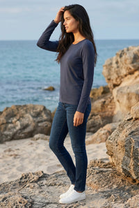 Woman in steel blue long sleeve Pima cotton tee and jeans standing on a rocky beach