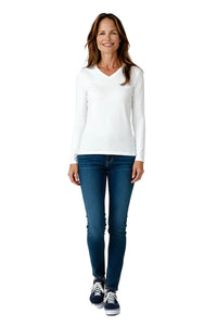 Smiling woman wearing white long-sleeve V-neck shirt, blue jeans, and navy sneakers on white background