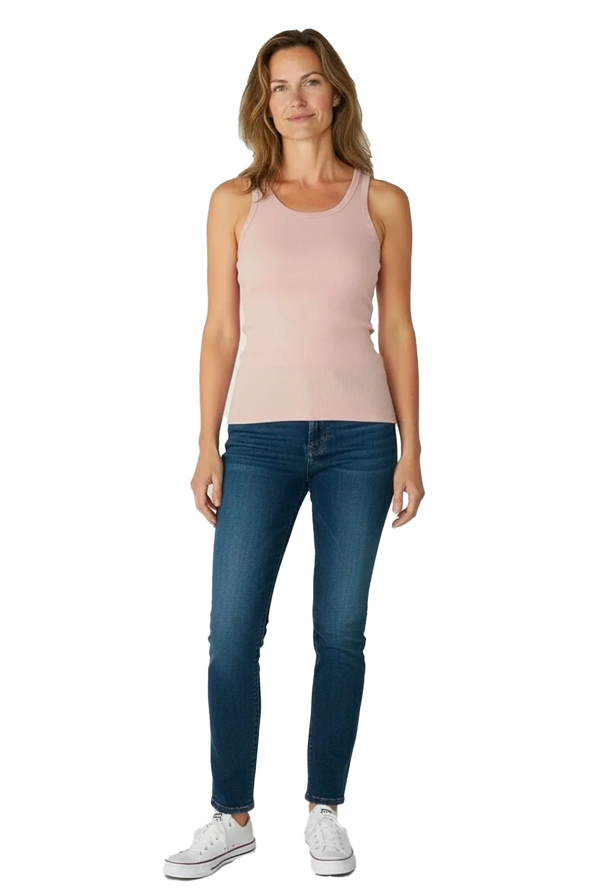 Woman wearing shell pink tank top, blue jeans, and white sneakers on white background