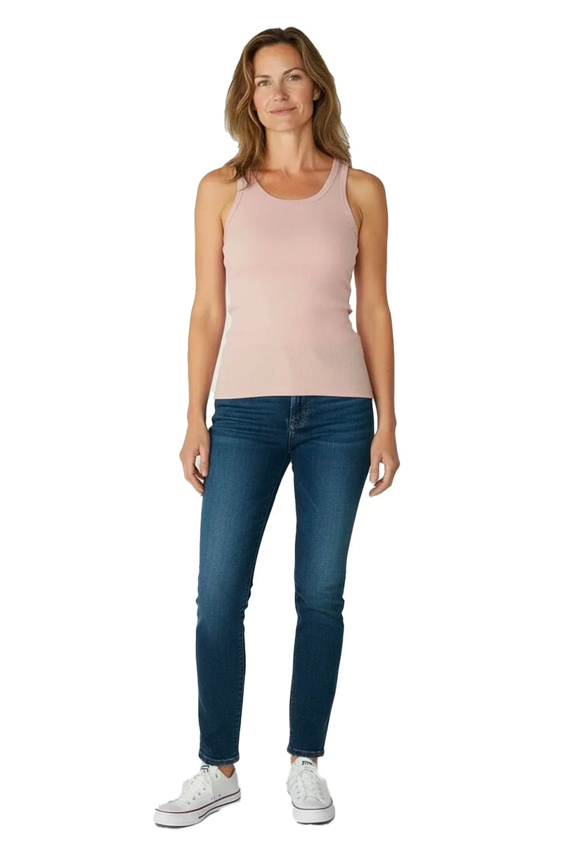 Woman wearing shell pink tank top, blue jeans, and white sneakers on white background