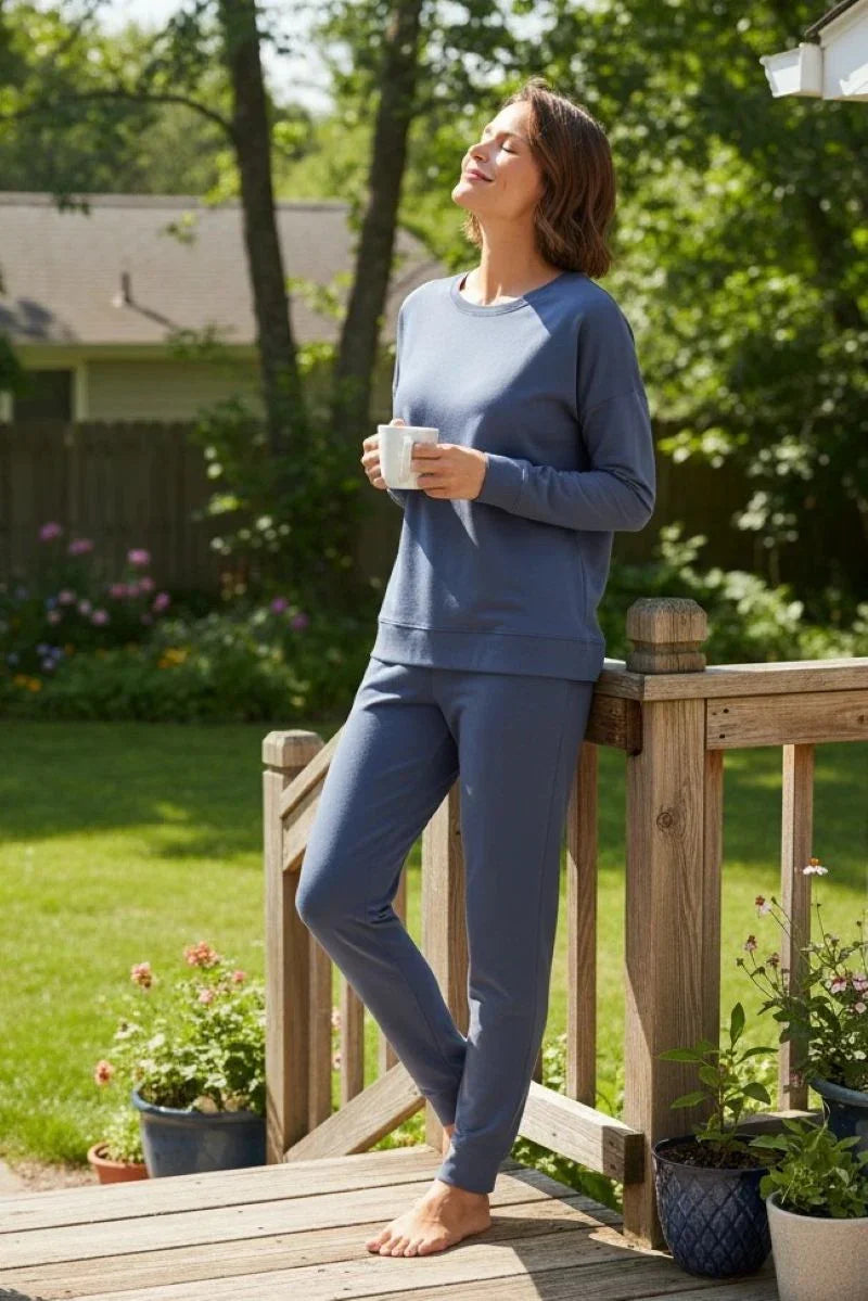Woman in steel blue loungewear holding mug, relaxing barefoot on wooden porch in sunny garden