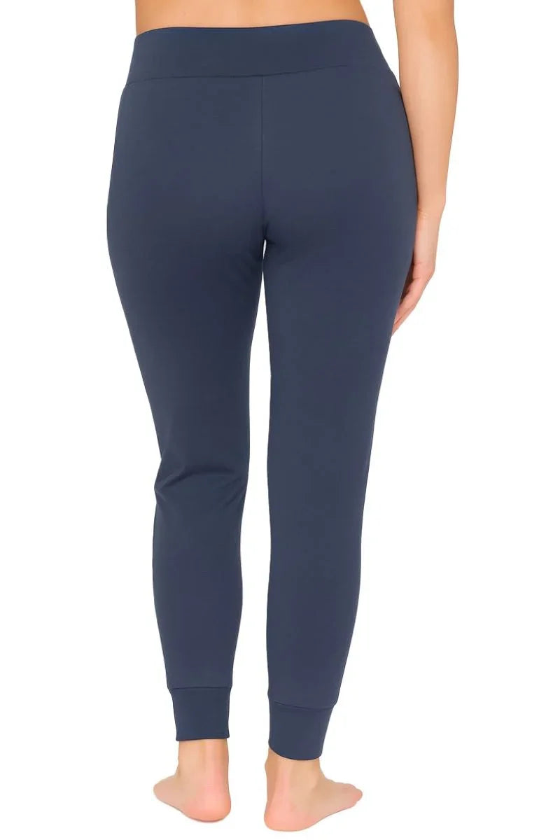 Back view of woman wearing steel blue fitted jogger pants with cuffed ankles, barefoot on white background